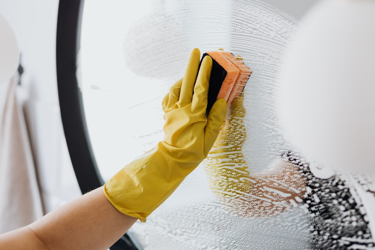 about-02 An unidentified person wearing yellow rubber gloves cleaning a bathroom mirror with a basic sponge